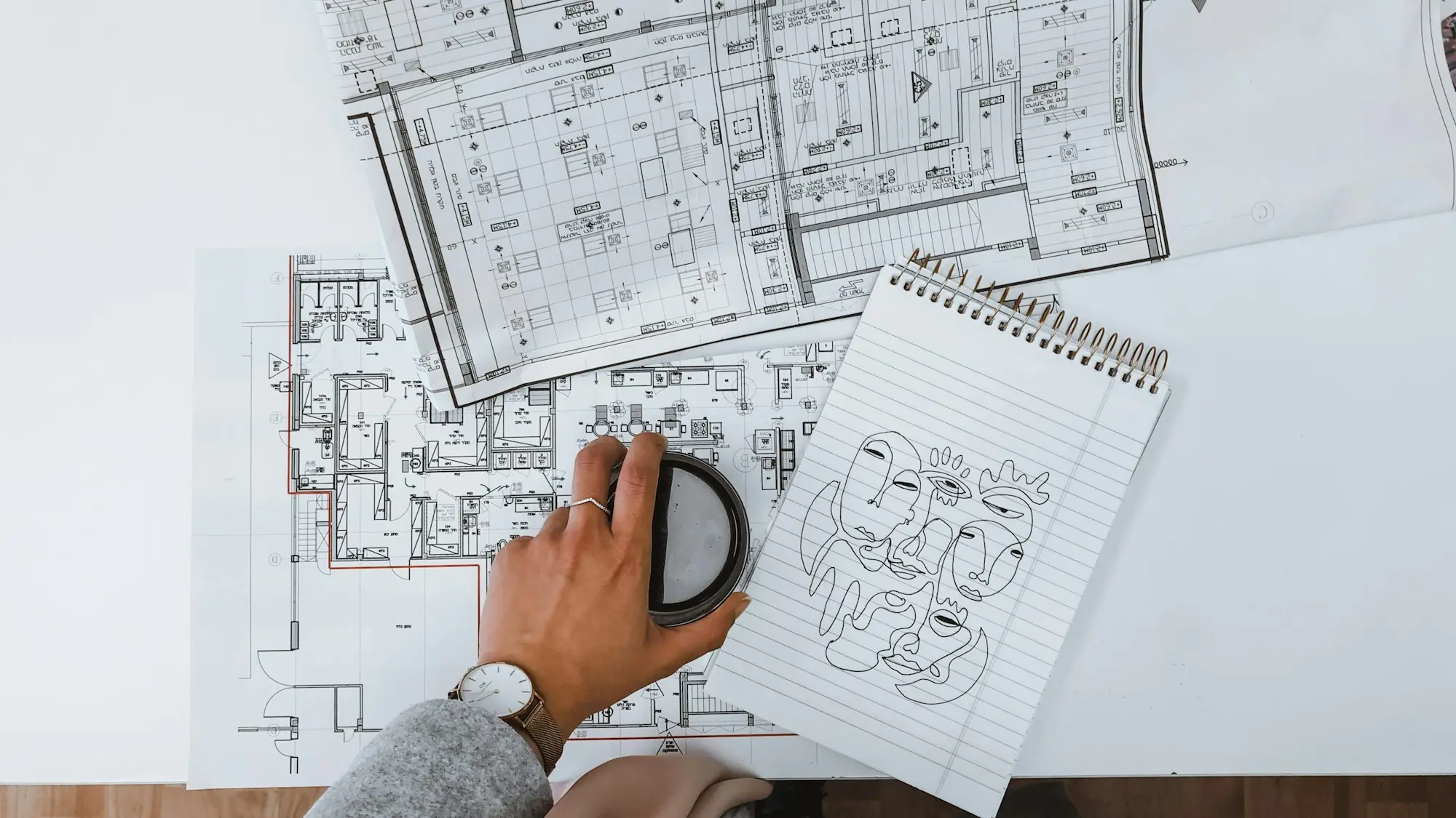 Hand resting on architectural floor plans for a shop tenancy beside a sketch notebook while a change of use approval is pending